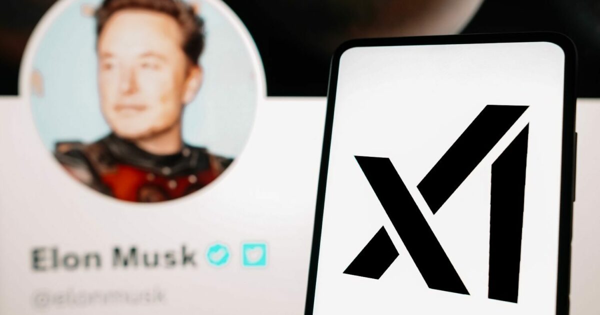 Imagem mostrando um smartphone com o logotipo da xAI, empresa de inteligência artificial de Elon Musk. Ao fundo, há um perfil desfocado do empresário Elon Musk em uma rede social