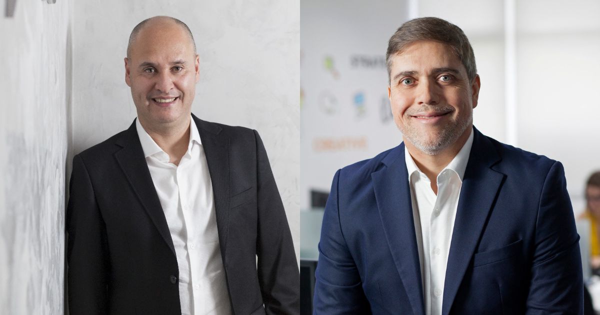 A imagem mostra dois executivos da empresa Objective. À esquerda, Paulo Miranda, CEO da Objective, aparece sorrindo e com um traje formal, utilizando um blazer preto e camisa branca. À direita, Jorge Sellmer, CRO da Objective, também sorri, vestindo um terno azul e camisa branca. O ambiente de fundo é moderno, com elementos que sugerem um escritório corporativo. Ambos estão posicionados de forma que destacam a personalidade de cada um, com um clima profissional e acolhedor.