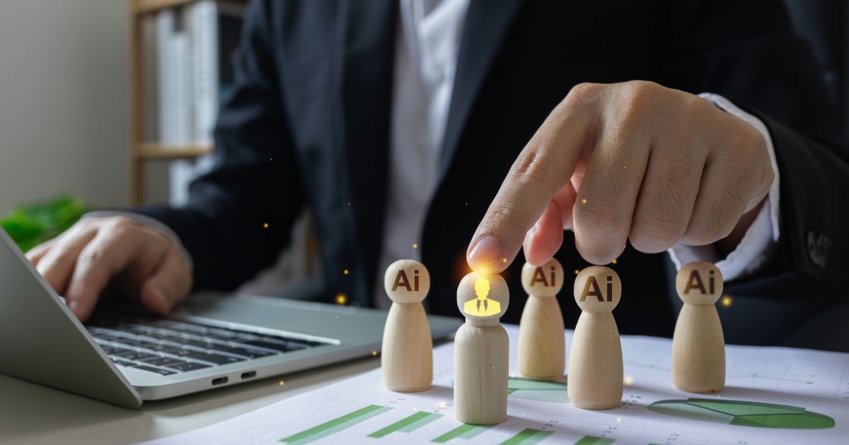 Uma pessoa vestida de terno preto, usando um laptop enquanto toca em uma peça de madeira que simboliza uma figura humana. Ao redor, há outras peças similares com a inscrição 'AI' no topo. A peça tocada está iluminada, destacando-se como um foco de atenção. No fundo, um ambiente de escritório com prateleiras e documentos.