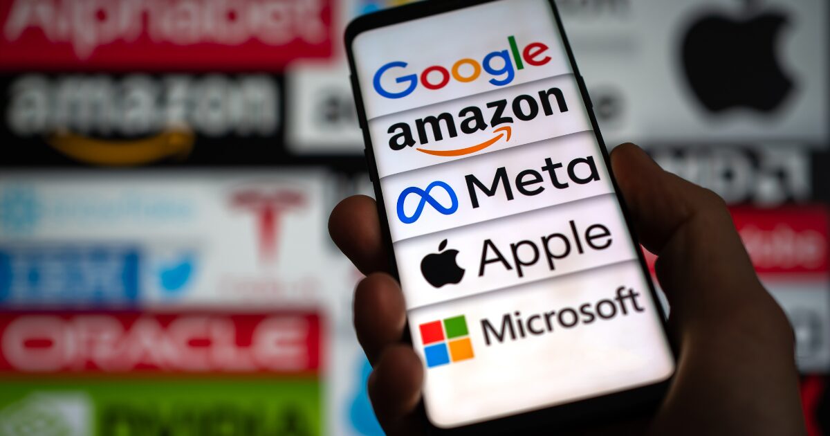 Imagem de um smartphone exibindo os logotipos de grandes empresas de tecnologia, como Google, Amazon, Meta, Apple e Microsoft, em destaque na tela. Ao fundo, desfocado, estão os logos. (big techs) Nasdaq