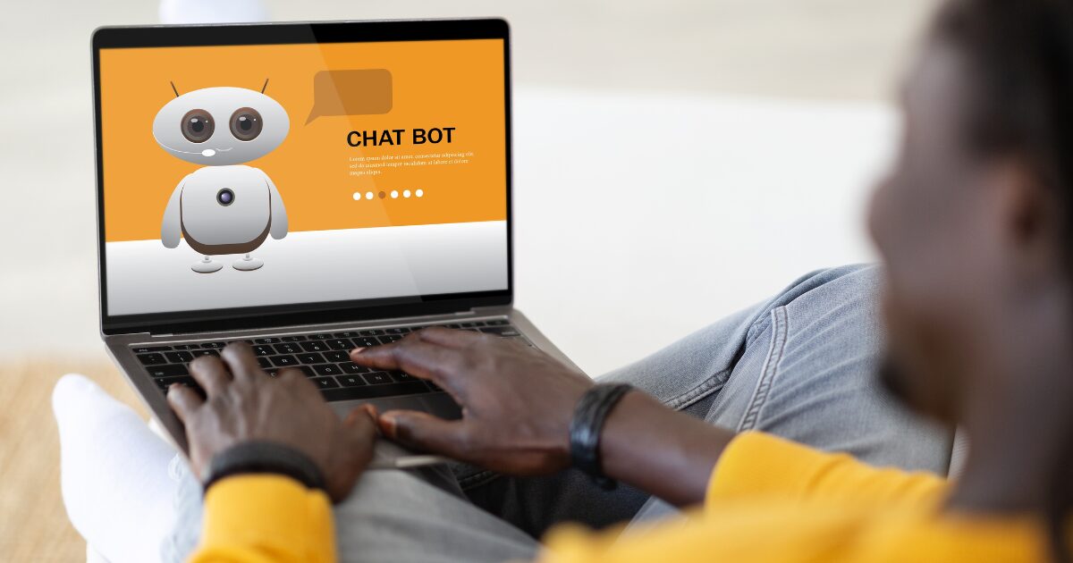 Pessoa usando um notebook, onde aparece na tela uma interface do chatbot. O chatbot é representado por um robô animado com grandes olhos e um corpo branco e cinza em um fundo laranja, acompanhado do texto “CHAT BOT” e um pequeno parágrafo em letras menores. A pessoa está sentada confortavelmente com roupas casuais, usa uma blusa amarela e calça jeans, interagindo