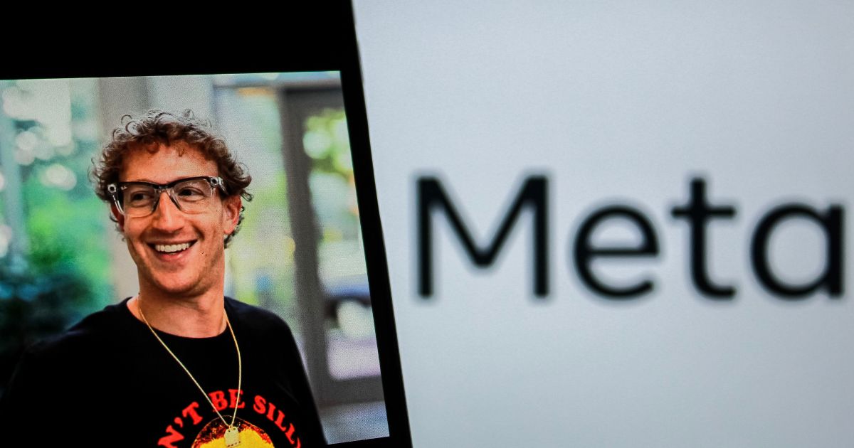 Uma fotografia mostra um homem sorridente com cabelo encaracolado e óculos, vestido de forma casual, com uma camisa preta estampada com um texto colorido. Ao lado dele, parcialmente visível, está o logótipo da empresa "Meta" sobre um fundo branco. A imagem combina o rosto do homem em destaque e o nome da empresa em plano de fundo.