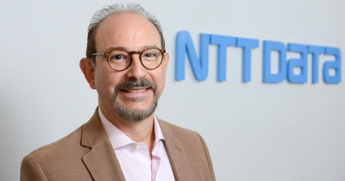 Ricardo Neves, CEO da NTT Data, sorrindo para a câmera em frente ao logotipo da empresa exibido na parede ao fundo (funcionários, ia generativa, inteligência artificial)