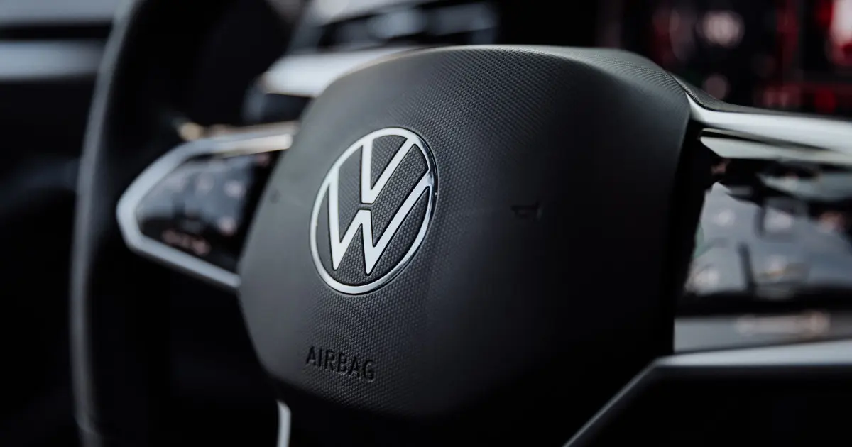 Logotipo da Volkswagen no centro do volante de um carro, com detalhes internos do veículo ao fundo