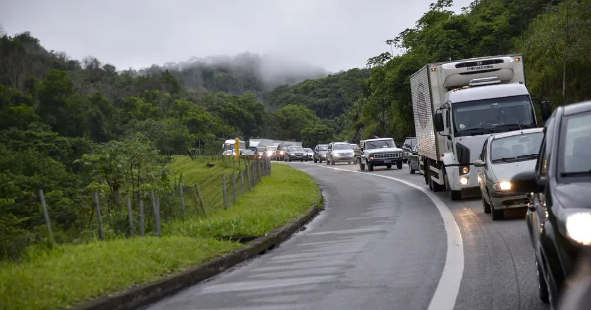 Tráfego intenso em uma estrada sinuosa cercada por vegetação densa, com veículos leves e caminhões em um dia nublado (estrada, rodovia, carros, trânsito)