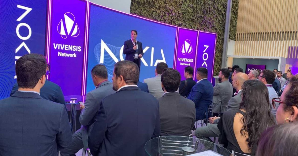 Evento oficial de anúncio da parceria entre Vivensis Network e Nokia, com um representante apresentando em um palco com as marcas destacadas ao fundo e uma plateia atenta