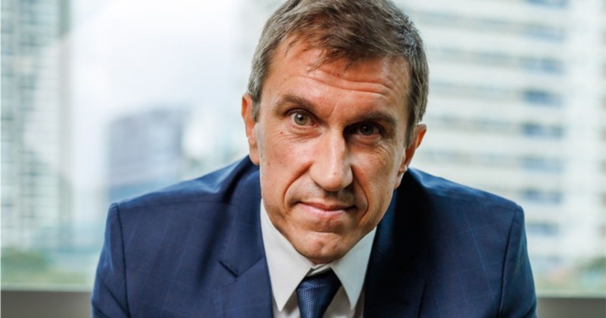 Retrato de Mauricio Arrausi, ex-CIO da Cofco Internacional. Ele veste um terno azul-escuro, camisa branca e gravata azul, e tem uma expressão séria. O fundo da imagem mostra prédios modernos, sugerindo um ambiente corporativo ou urbano