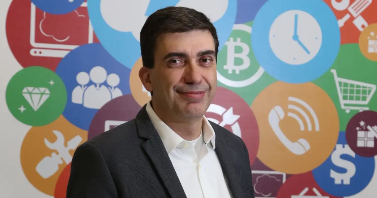 Retrato de Maurício Fernandes, CEO da Dedalus, vestindo terno escuro e camisa branca. Ele está em frente a um fundo colorido com ícones que representam tecnologia, como relógio, bitcoin e telefone, transmitindo uma atmosfera inovadora e tecnológica (tendências)