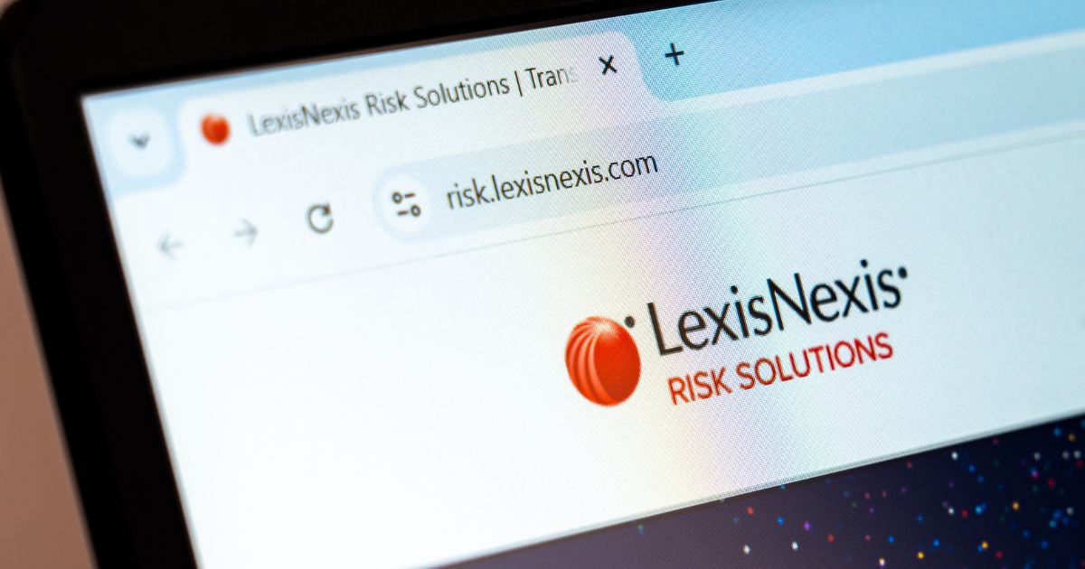 Fotografia de um ecrã de computador exibindo o site 'LexisNexis Risk Solutions'. A aba do navegador mostra o título parcial da página e o URL 'risk.lexisnexis.com'. O logótipo da empresa, que inclui um ícone vermelho esférico e o nome 'LexisNexis' em preto, seguido de 'RISK SOLUTIONS' em vermelho, está visível. O fundo do site contém um design com pequenos pontos coloridos sobre um fundo escuro. A imagem está levemente inclinada, capturando a tela em perspectiva.