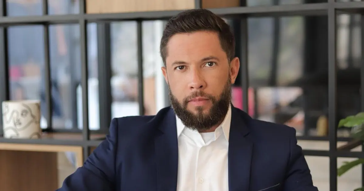 Retrato de Paulo Silvestre, diretor de inovação e desenvolvimento estratégico do ButtiniMoraes, usando um terno azul e camisa branca. Ele está sentado em um ambiente moderno, com prateleiras ao fundo, transmitindo um ar de seriedade e profissionalismo (plataforma)