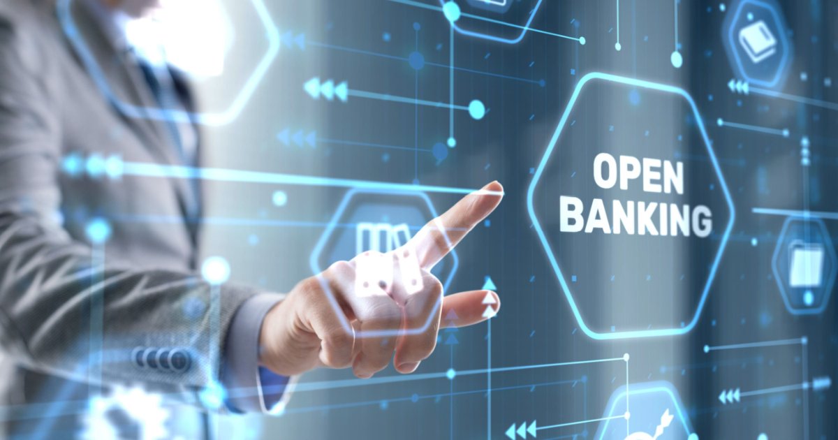 Imagem conceitual sobre Open Banking. Uma mão apontando para um painel digital com o texto 'OPEN BANKING' destacado em um hexágono luminoso. O fundo apresenta ícones tecnológicos e conexões digitais em tons de azul, representando a integração e o compartilhamento de dados financeiros de forma segura e transparente, consentimentos